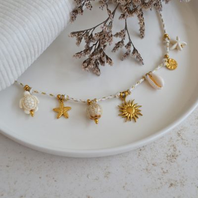 Collier en acier inoxydable avec chaine en cordon blanc orné de sept pendentifs dorés et blancs esprit vacances à la plage.