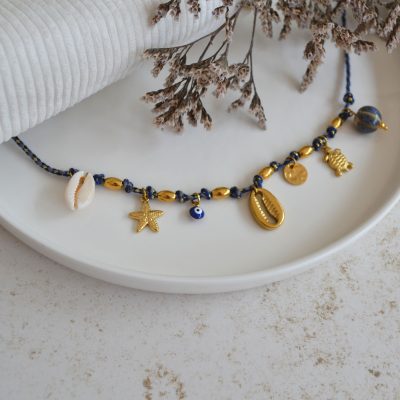 Collier en acier inoxydable avec chaine en cordon bleu marine orné de sept pendentifs dorés et bleu marine esprit vacances à la plage.
