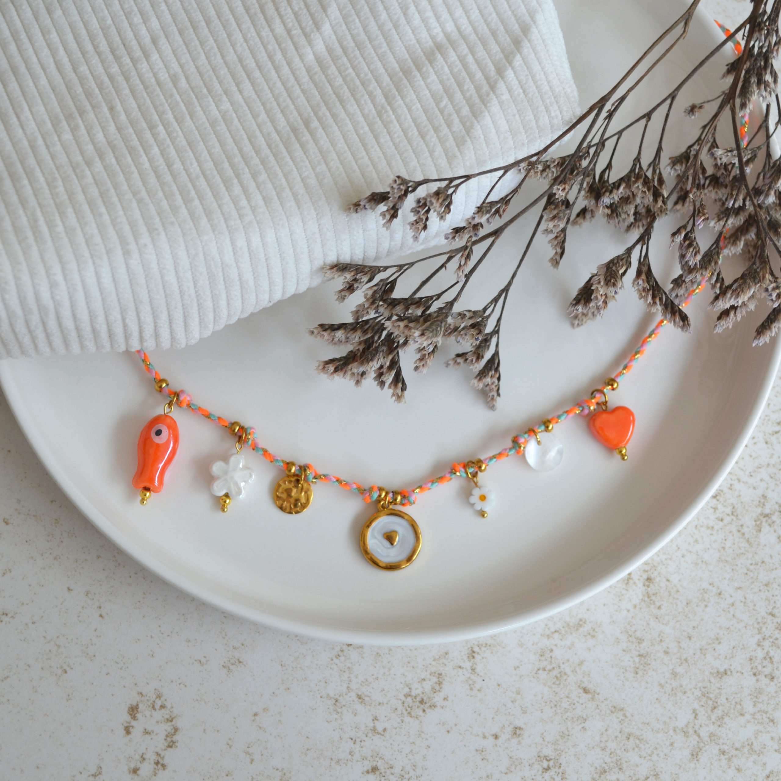 Collier en acier inoxydable avec chaine en cordon orange orné de sept pendentifs dorés et orange esprit estival.