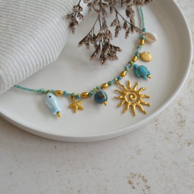 Collier en acier inoxydable avec chaine en cordon bleu orné de sept pendentifs dorés et bleus esprit vacances à la plage.