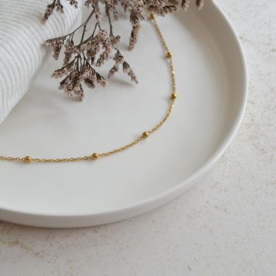 Collier en acier inoxydable avec chaine fine orné de petits ronds dorés esprit élégant.