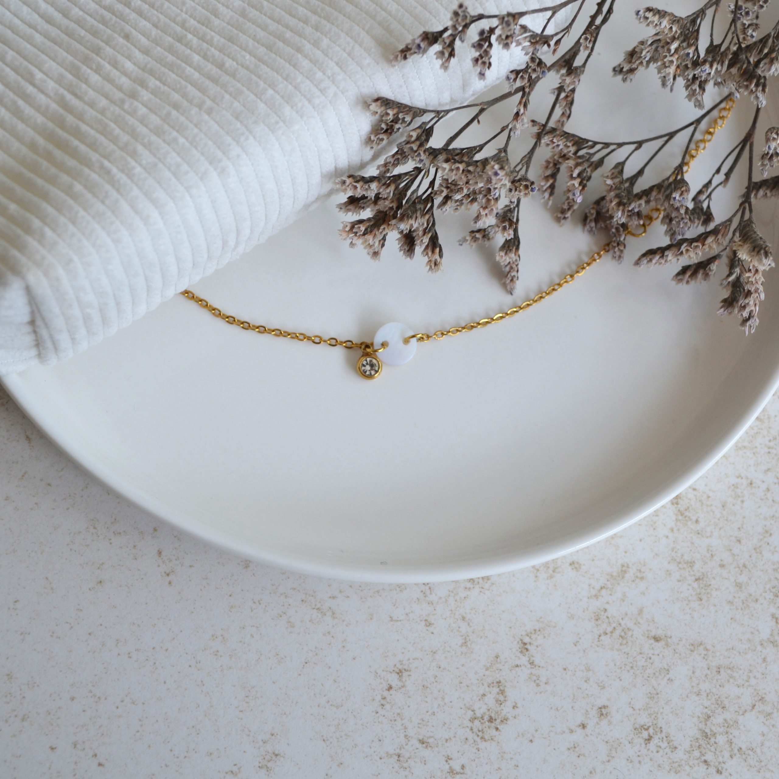 Bracelet en acier inoxydable avec chaine fine orné de pendentifs dorés et blanc esprit élégant.
