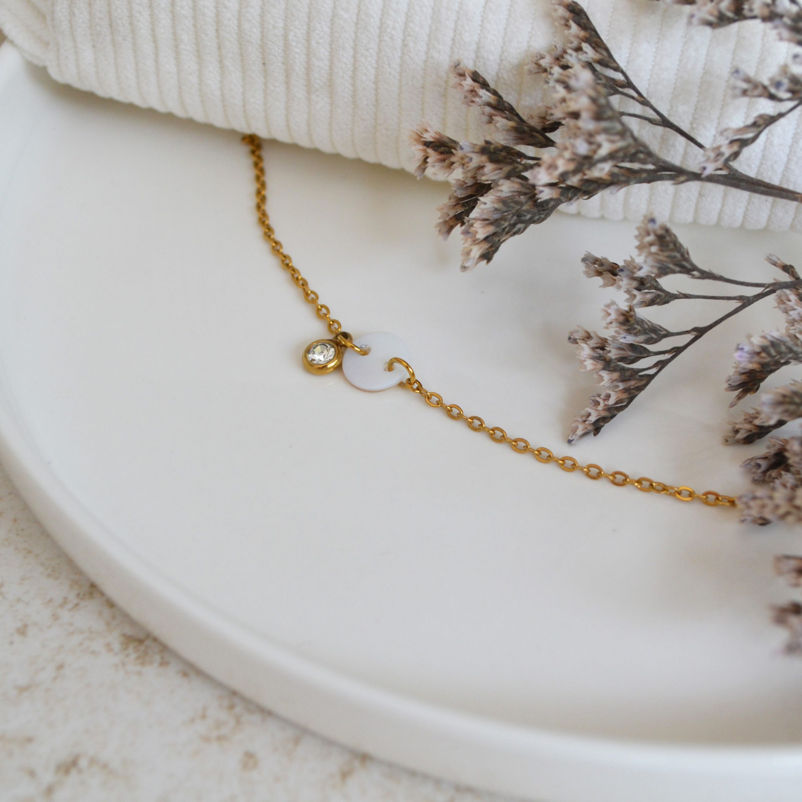 Bracelet en acier inoxydable avec chaine fine orné de pendentifs dorés et blanc esprit élégant.