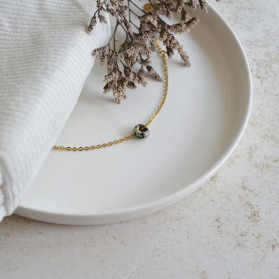 Bracelet en acier inoxydable avec chaine fine dorée orné d'un pendentif en forme de perle tachetée.