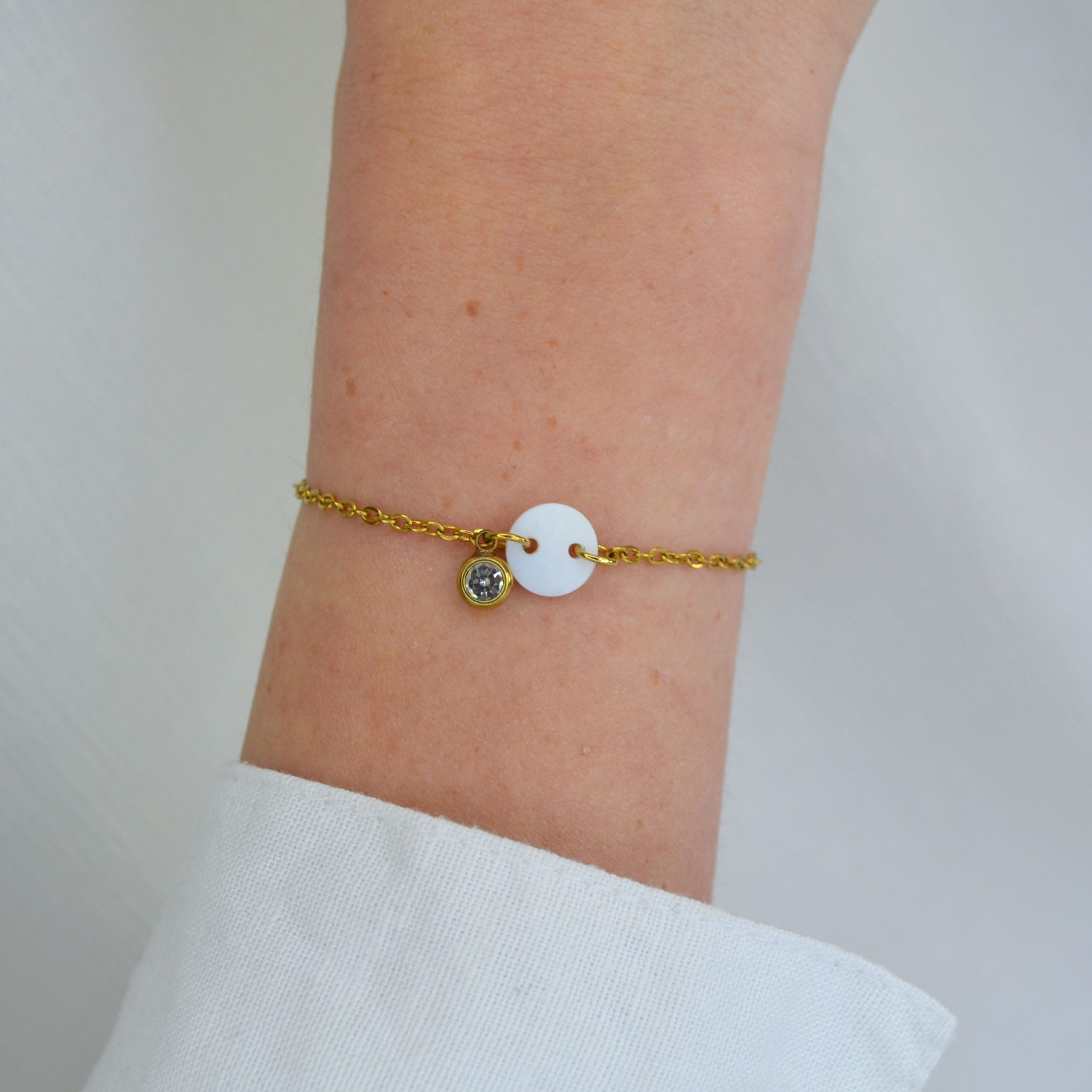 Bracelet en acier inoxydable avec chaine fine orné de pendentifs dorés et blanc esprit élégant.