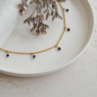Collier en acier inoxydable avec chaine fine dorée orné de cinq petites pierres noires esprit élégant.