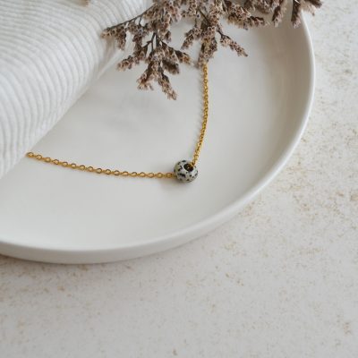Collier en acier inoxydable avec chaine fine dorée orné d'un pendentif en forme de perle grise et noire.