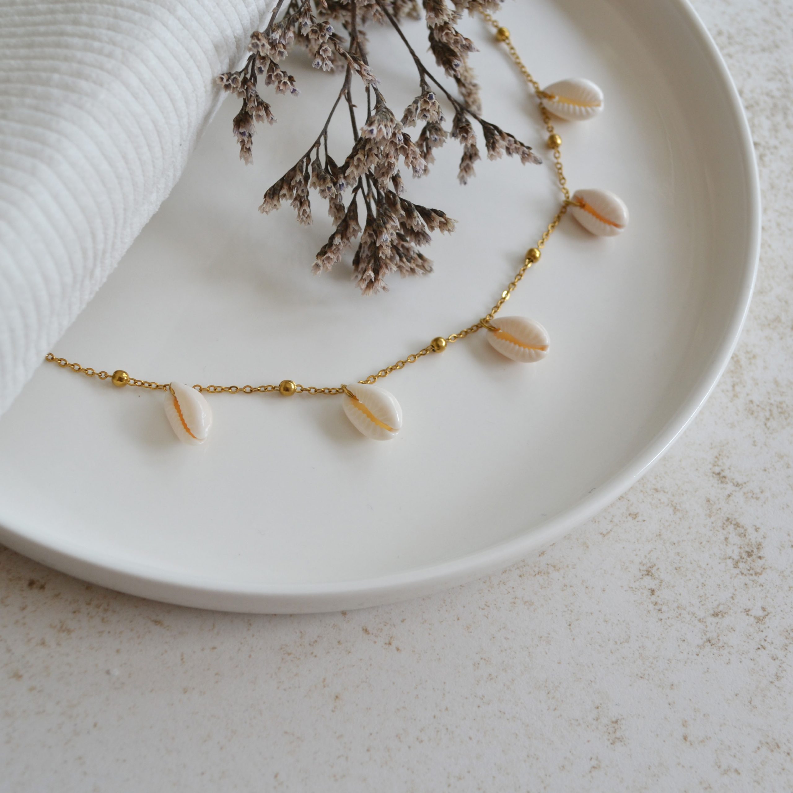 Bracelet de cheville en acier inoxydable avec chaine fine dorée orné de coquillage esprit vacances à la plage.