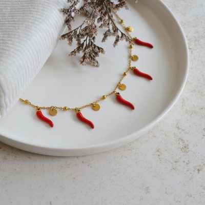 Bracelet de cheville en acier inoxydable avec chaine fine dorées ornée de pendentifs en forme de piments rouges.