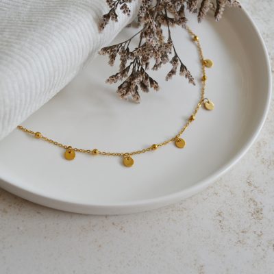 Bracelet de cheville en acier inoxydable avec chaine fine dorée ornée de pendentifs ronds lisses.