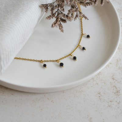 Bracelet en acier inoxydable avec chaine fine dorée orné de cinq petites pierres noires esprit élégant.